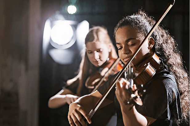Two musicians playing violins in spotlight.
