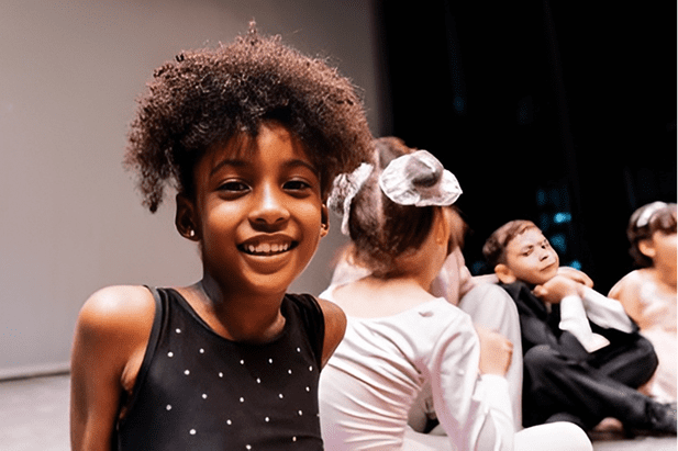 Children smiling on a stage during rehearsal.